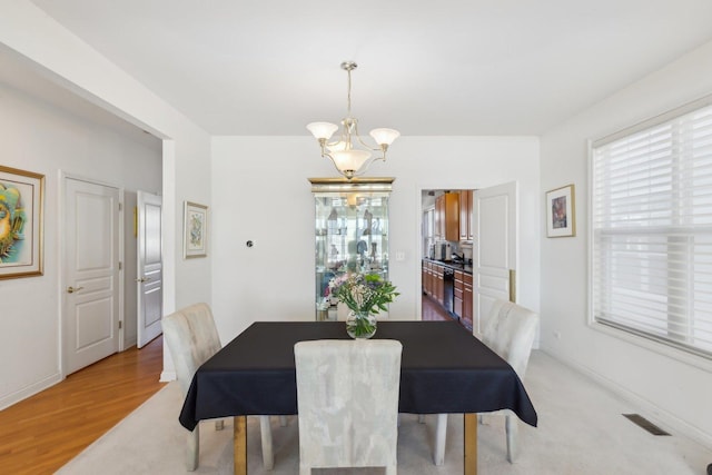 dining room with baseboards, light wood-style floors, visible vents, and a notable chandelier