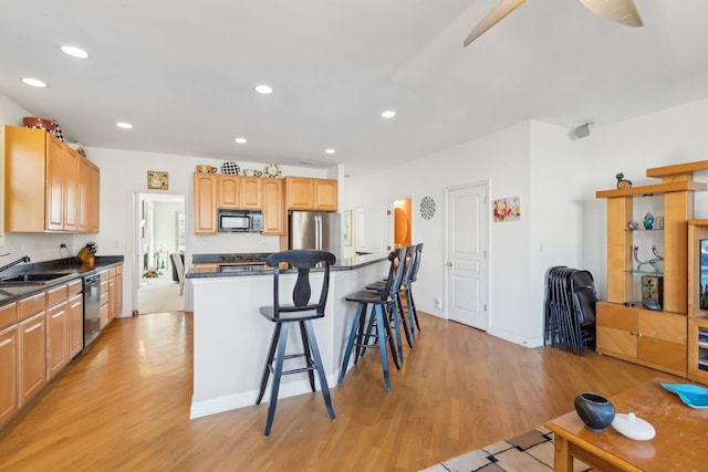 kitchen featuring light wood-style flooring, a breakfast bar, a kitchen island, appliances with stainless steel finishes, and dark countertops