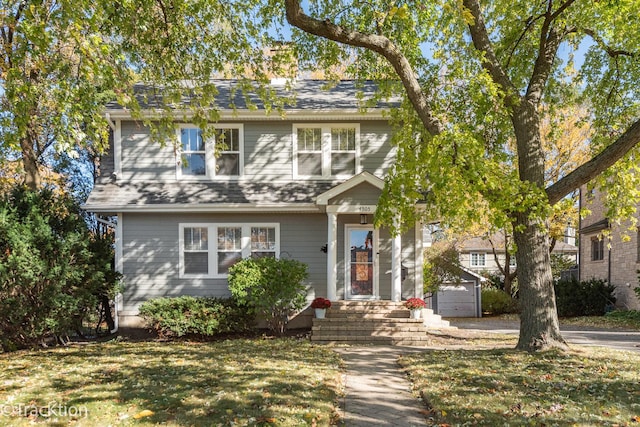 view of front of house featuring a shingled roof, a front yard, and an outdoor structure