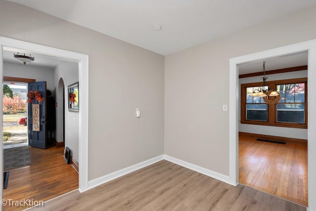 unfurnished room with arched walkways, visible vents, an inviting chandelier, wood finished floors, and baseboards