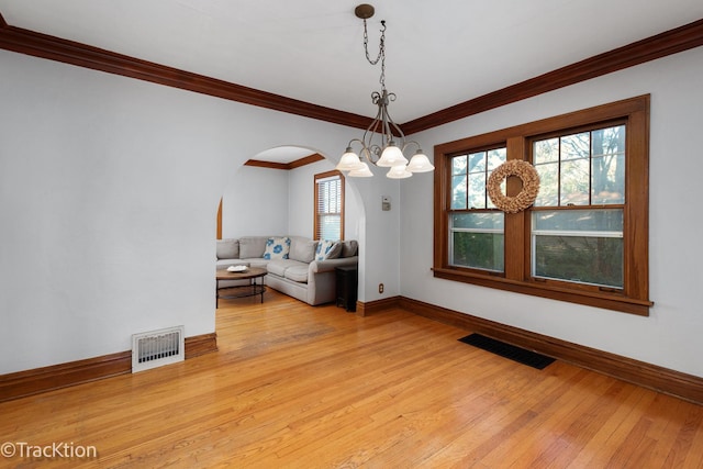 unfurnished living room featuring light wood-style floors, arched walkways, visible vents, and baseboards