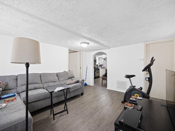 living area featuring arched walkways, dark wood-type flooring, a textured ceiling, and visible vents