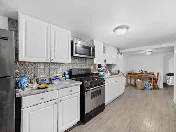 kitchen featuring appliances with stainless steel finishes, decorative backsplash, white cabinetry, and light wood-style floors