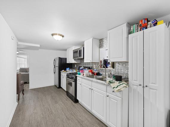 kitchen with light wood finished floors, stainless steel appliances, light countertops, decorative backsplash, and white cabinetry