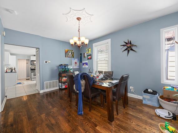 dining space with baseboards, wood finished floors, visible vents, and a notable chandelier