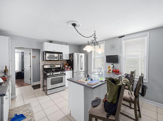 kitchen featuring white cabinets, dark countertops, appliances with stainless steel finishes, pendant lighting, and light tile patterned flooring