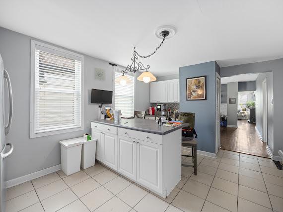 kitchen featuring pendant lighting, dark countertops, white cabinetry, light tile patterned flooring, and a peninsula