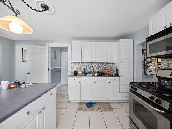 kitchen featuring stainless steel appliances, dark countertops, tasteful backsplash, white cabinets, and a sink