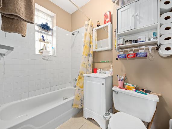 full bath featuring toilet, tile patterned flooring, shower / bathtub combination with curtain, and a sink