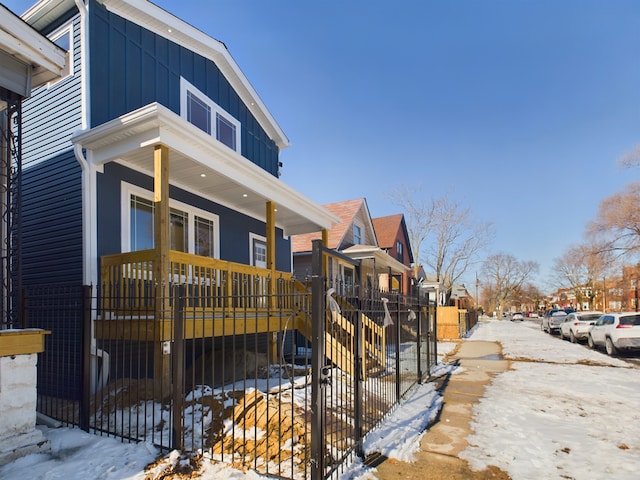 view of snowy exterior with a residential view, fence, a porch, and board and batten siding