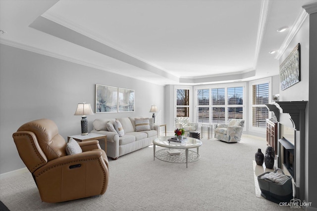 living area with baseboards, a fireplace with raised hearth, a raised ceiling, ornamental molding, and carpet floors