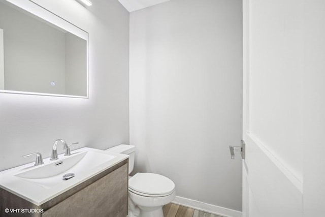 half bathroom featuring baseboards, vanity, toilet, and wood finished floors