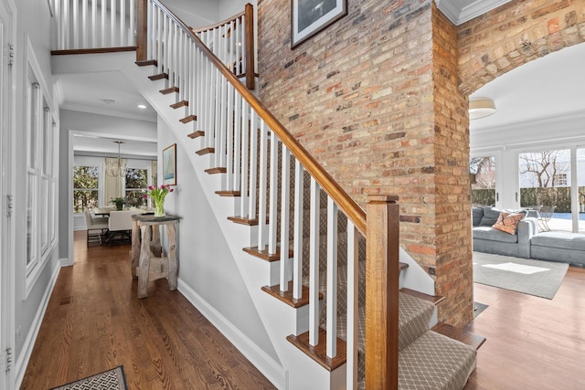 staircase featuring brick wall, a high ceiling, wood finished floors, baseboards, and ornamental molding