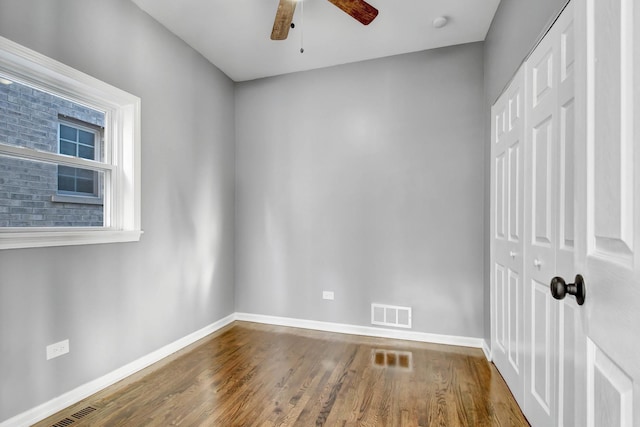 unfurnished room with ceiling fan, wood finished floors, visible vents, and baseboards