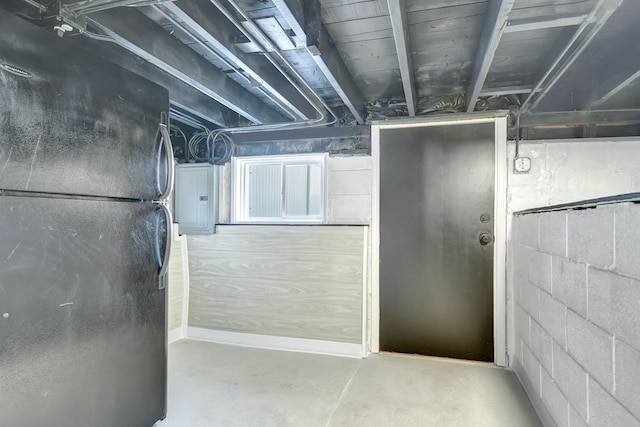 unfinished basement featuring freestanding refrigerator, electric panel, and concrete block wall