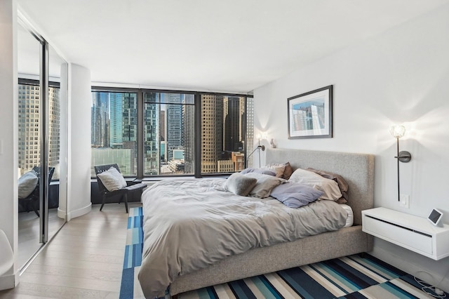 bedroom featuring a view of city, multiple windows, light wood-type flooring, and a wall of windows