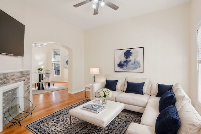 living room featuring arched walkways, baseboards, a ceiling fan, and light wood-style floors