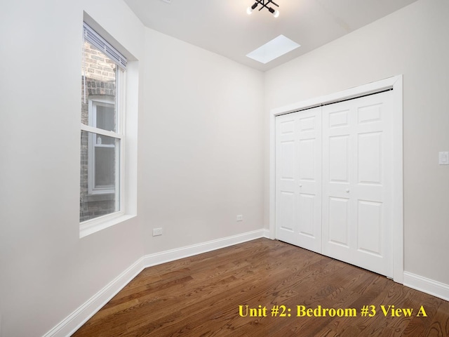 unfurnished bedroom featuring a closet, a skylight, dark wood-style flooring, and baseboards