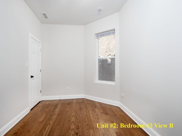 unfurnished room with wood finished floors, visible vents, and baseboards