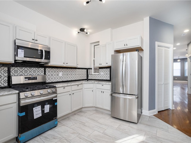 kitchen featuring baseboards, white cabinets, appliances with stainless steel finishes, backsplash, and light stone countertops