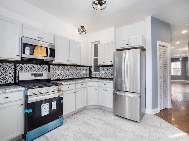 kitchen featuring light stone counters, decorative backsplash, appliances with stainless steel finishes, white cabinetry, and baseboards