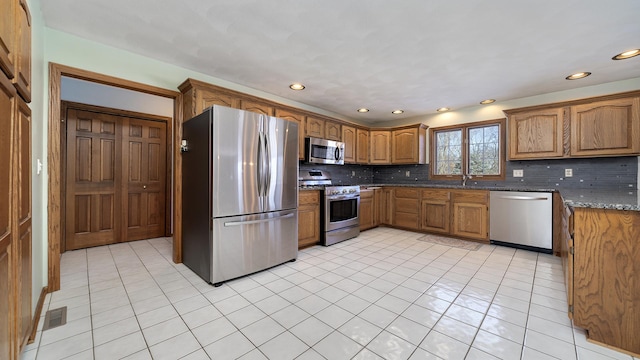 kitchen featuring appliances with stainless steel finishes, brown cabinetry, backsplash, and dark stone countertops