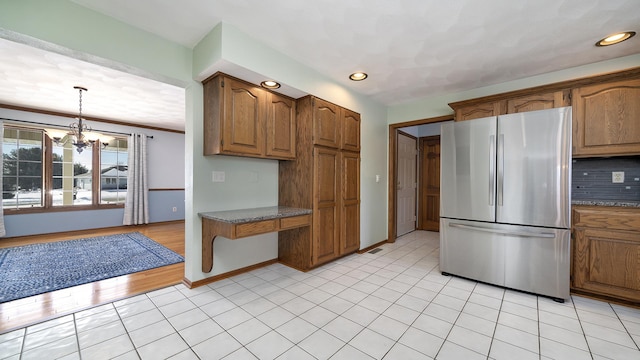 kitchen with brown cabinetry, decorative backsplash, freestanding refrigerator, and decorative light fixtures