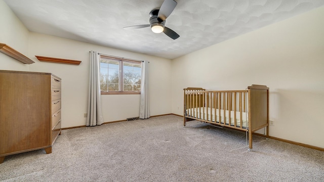 unfurnished bedroom featuring light carpet, visible vents, baseboards, a ceiling fan, and a nursery area