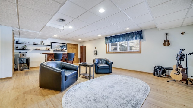 living room featuring light wood finished floors, beverage cooler, visible vents, a paneled ceiling, and a bar