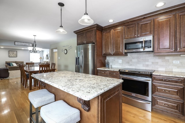 kitchen featuring backsplash, appliances with stainless steel finishes, a breakfast bar, and light wood-style floors