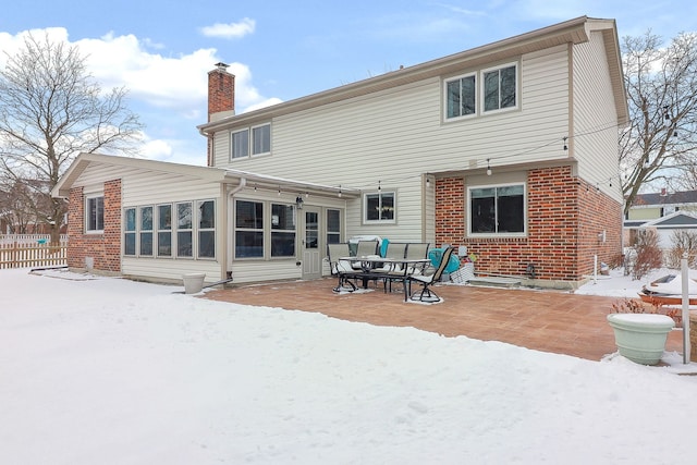 snow covered property featuring a patio, fence, brick siding, and a chimney