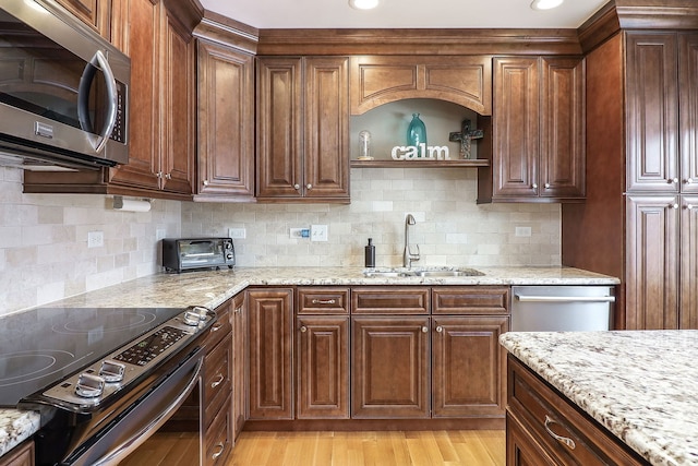 kitchen with light wood-style flooring, appliances with stainless steel finishes, light stone countertops, and a sink