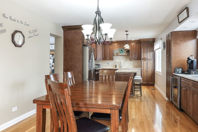 dining space with wine cooler, a notable chandelier, light wood-style floors, and baseboards