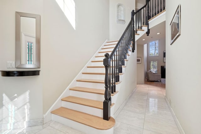 stairs with tile patterned flooring, a high ceiling, and baseboards