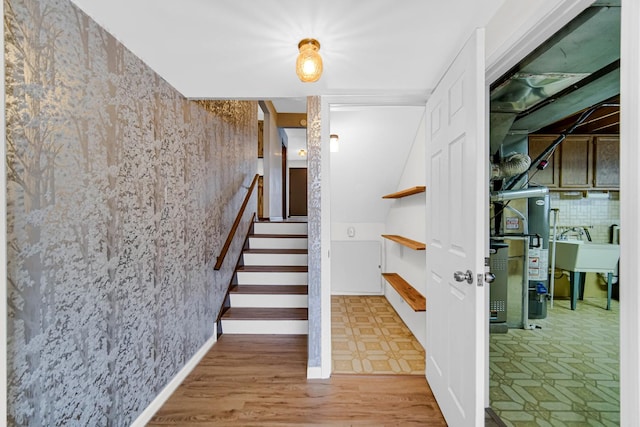 staircase featuring wood finished floors, gas water heater, baseboards, and wallpapered walls