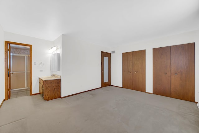 unfurnished bedroom with visible vents, baseboards, light colored carpet, two closets, and a sink