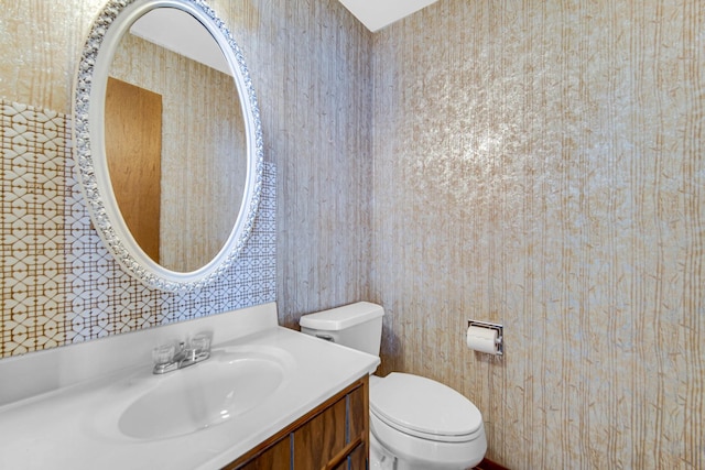 half bath with toilet, vanity, and wallpapered walls