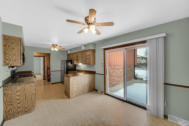 kitchen with visible vents, brown cabinetry, a sink, black appliances, and baseboards