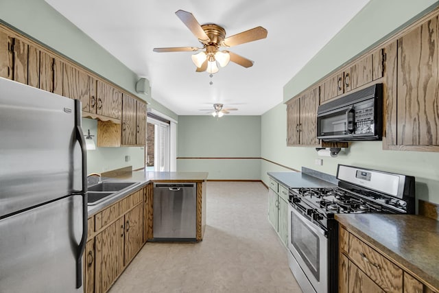 kitchen with a sink, appliances with stainless steel finishes, light floors, brown cabinetry, and dark countertops