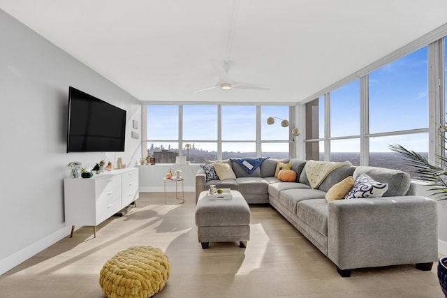 living area featuring light wood-type flooring, baseboards, and a ceiling fan