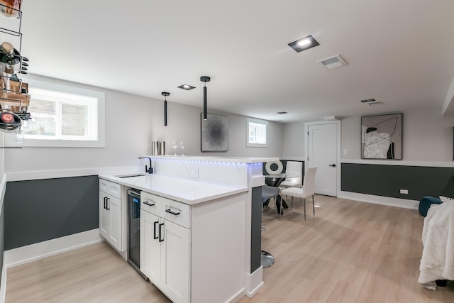 kitchen with beverage cooler, white cabinets, a peninsula, pendant lighting, and a sink