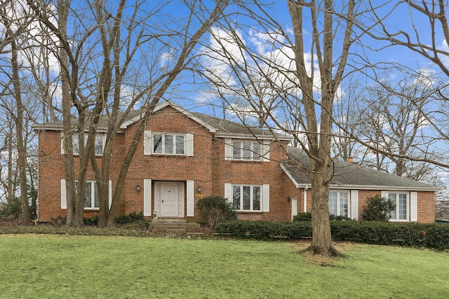 colonial-style house with a front yard, a chimney, and brick siding