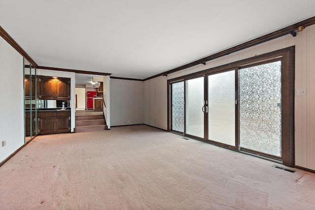 unfurnished living room featuring light carpet, stairway, visible vents, and crown molding