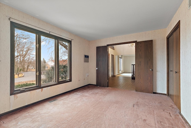 empty room with carpet floors, visible vents, and wallpapered walls