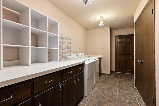 laundry area featuring brick floor, cabinet space, a sink, washer and dryer, and wallpapered walls