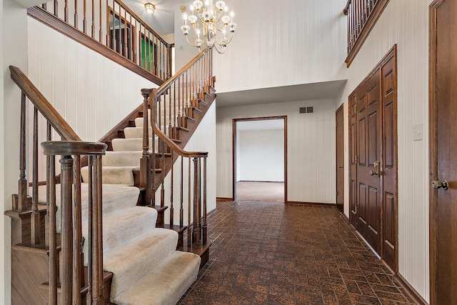 foyer entrance with baseboards, visible vents, brick floor, a high ceiling, and a chandelier