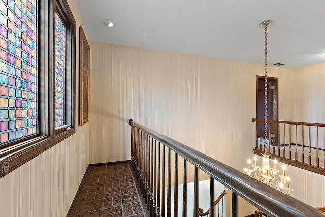 corridor featuring brick floor, visible vents, a notable chandelier, and an upstairs landing