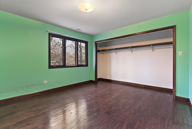 unfurnished bedroom featuring dark wood-style flooring, a closet, visible vents, and baseboards