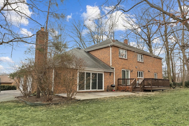 back of house featuring brick siding, a chimney, a lawn, a patio area, and a wooden deck