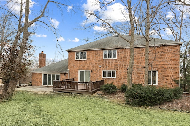 rear view of property with brick siding, a chimney, a lawn, a patio area, and a deck